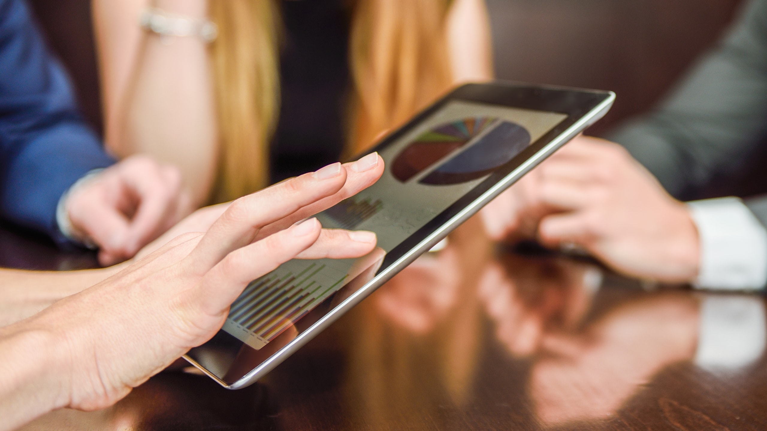 Mãos de mulher apontando gráficos em um tablet durante uma reunião com a equipe